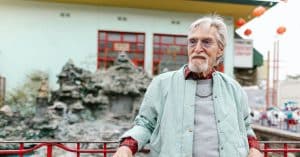 Oude man met ringbaard leunt tegen een rood hek