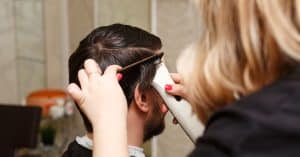 Vrouwelijke kapper geeft man een knip beurt met een professionele tondeuse en kam