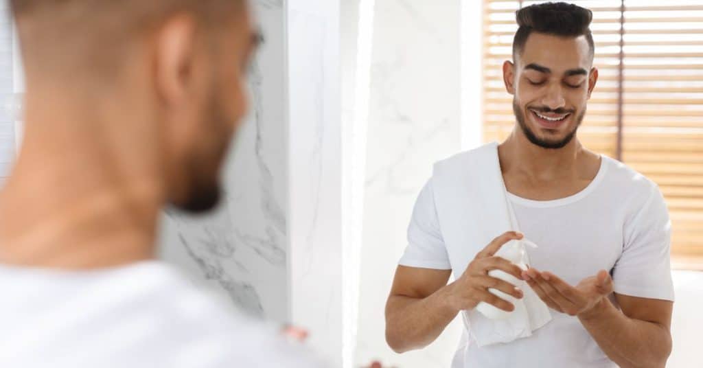 Man smeert voor de spiegel zijn gezicht in met Aftershavelotion
