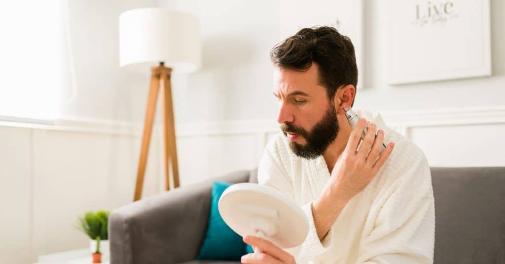 Man in badjas trimt voor een handspiegel zijn oorhaar