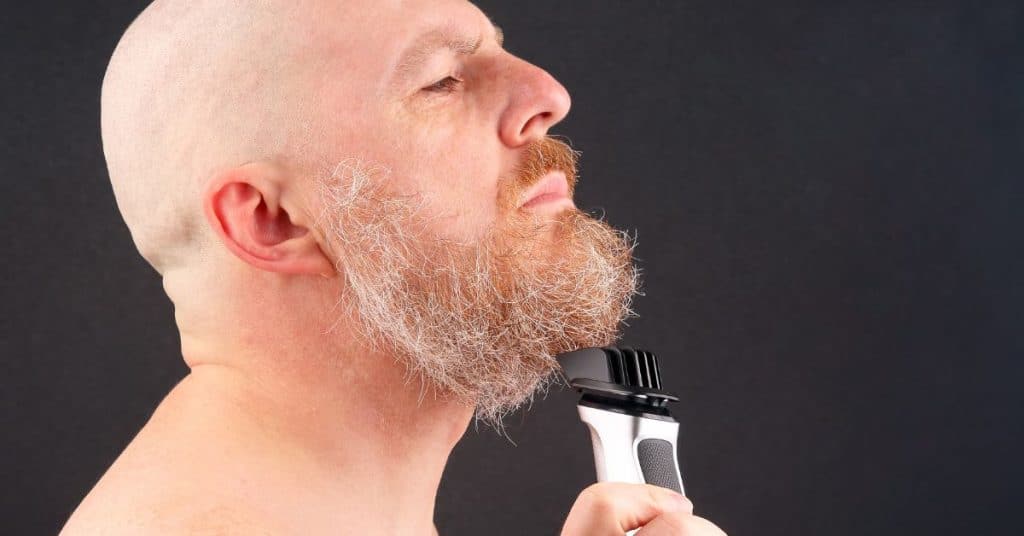 Man met kaal hoofd scheert zijn baard met een tondeuse