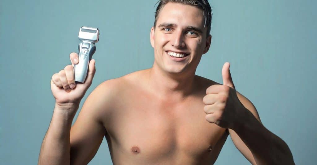 Man met ontbloot bovenlichaam met een scheerapparaat (multigroom) in zijn rechter hand (voor de kijkers links) en zijn duim omhoog in zijn linker hand (voor de kijkers rechts)