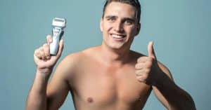 Man met ontbloot bovenlichaam met een scheerapparaat (multigroom) in zijn rechter hand (voor de kijkers links) en zijn duim omhoog in zijn linker hand (voor de kijkers rechts)